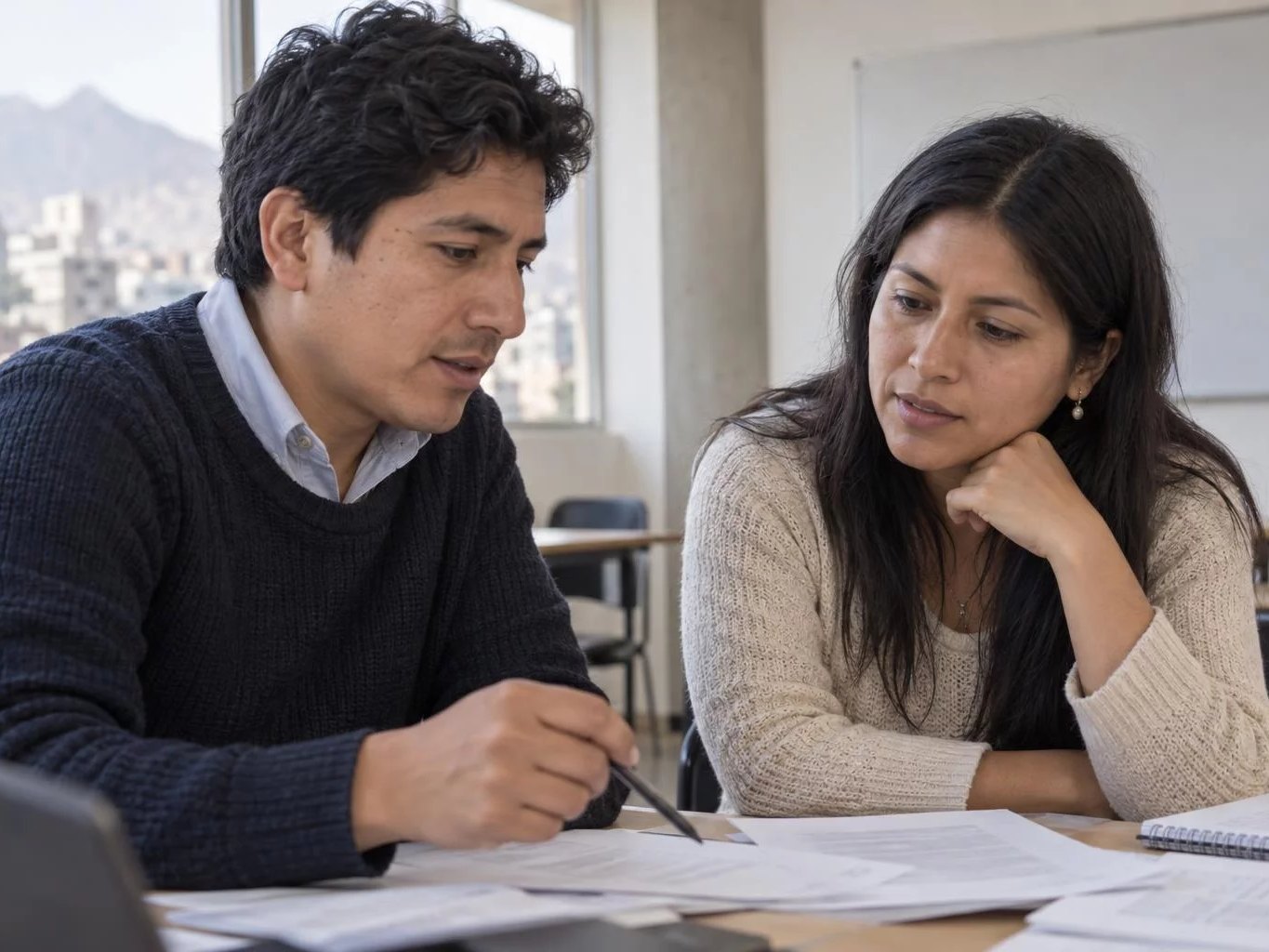 Dos adultos en una mesa de trabajo cubierta de apuntes impresos