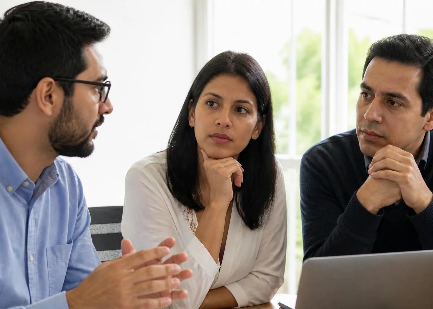 Tres profesionales en una sala de reuniones clara, uno de ellos explicando